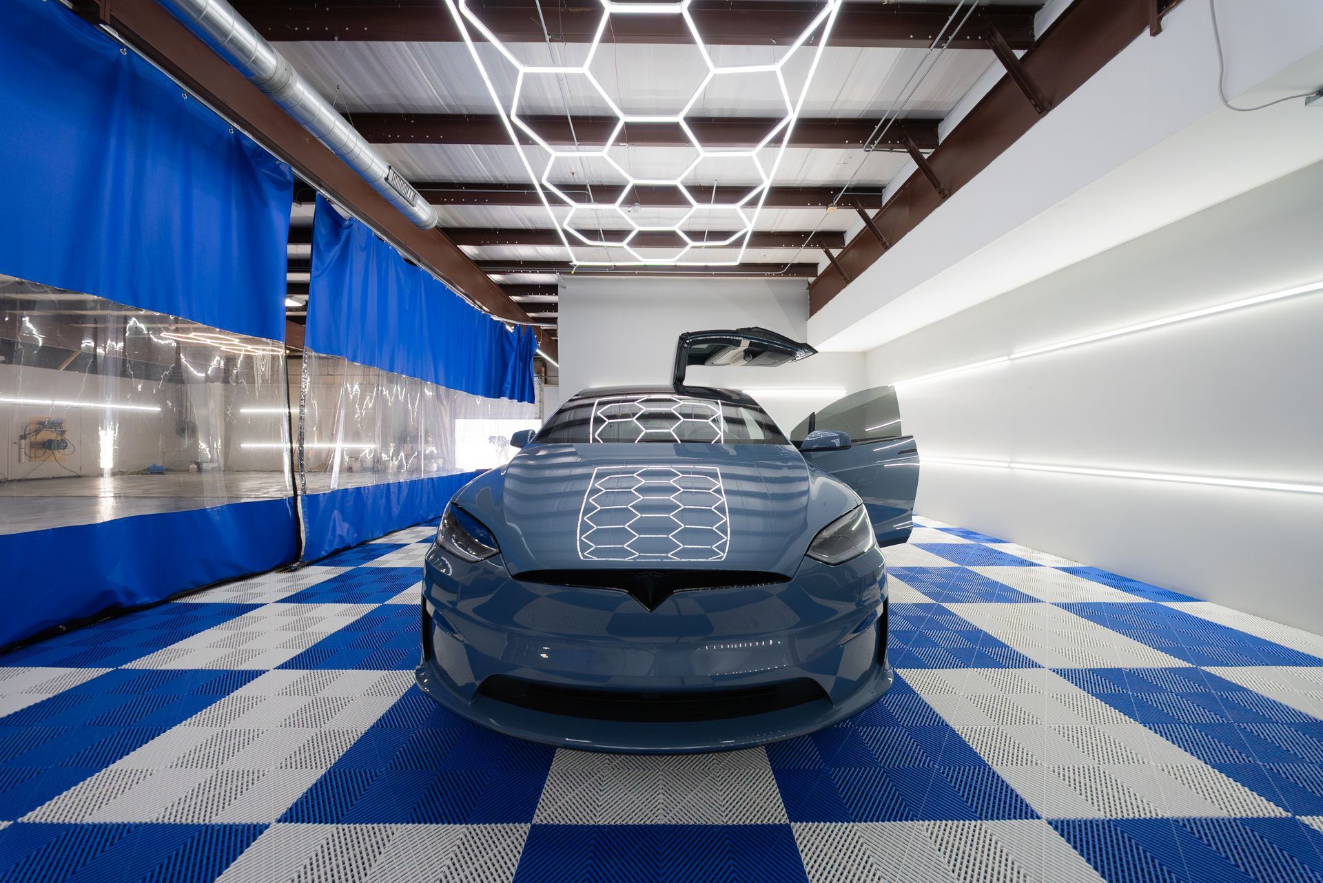 Blue car in a bright car wash bay with checkered floor tiles and overhead lights