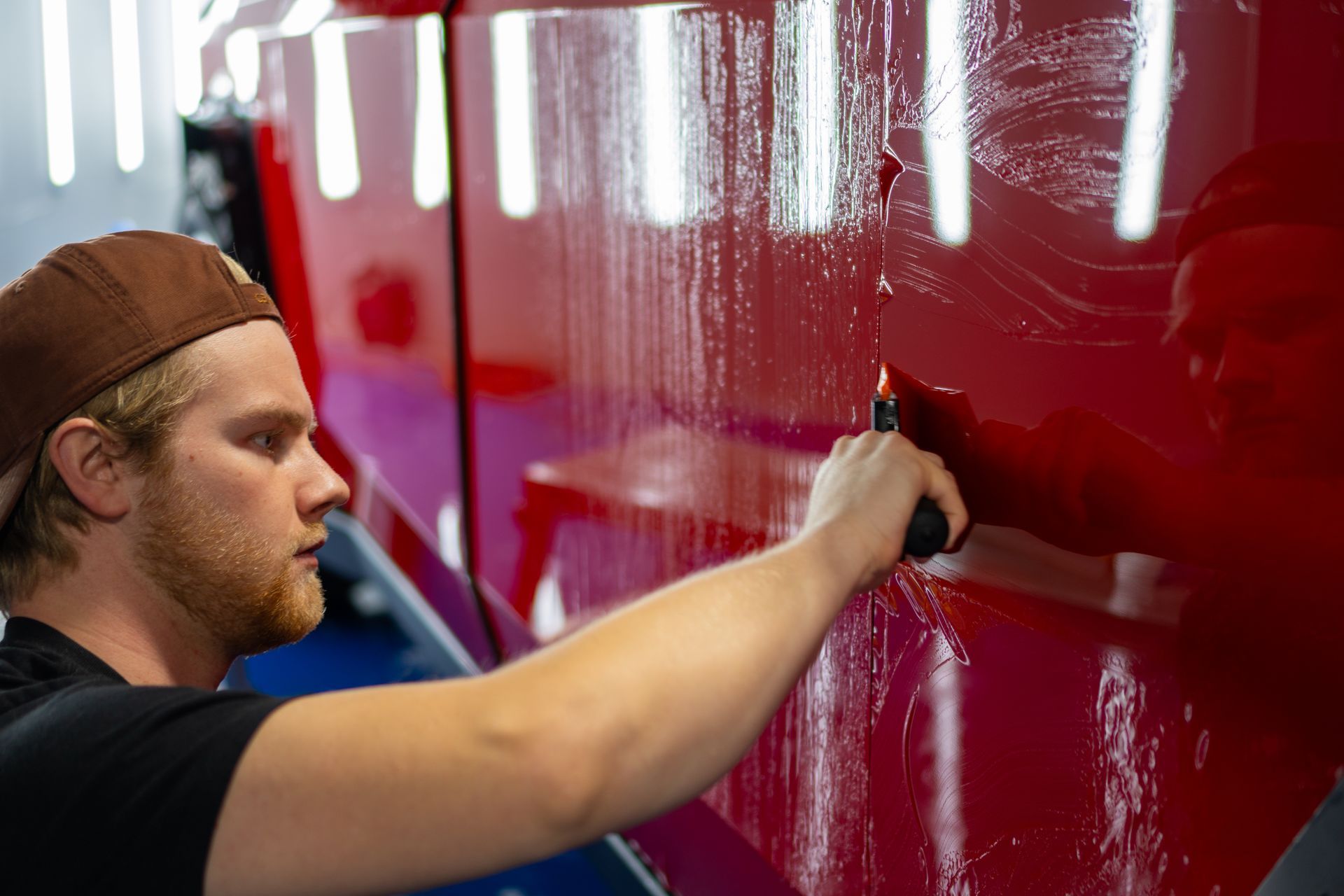 Person using a tool to apply film to a red surface. The person is in a garage or studio-like setting.