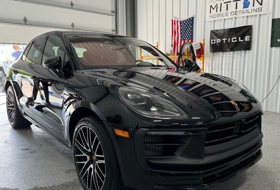 Black Porsche SUV in a garage with shop signage and an American flag