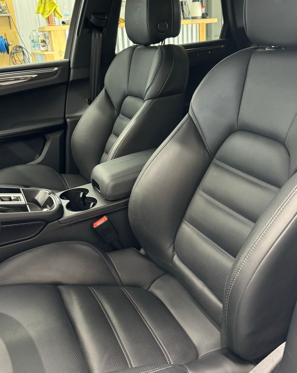 Black leather car seats with center console and quilted stitching in a vehicle interior.