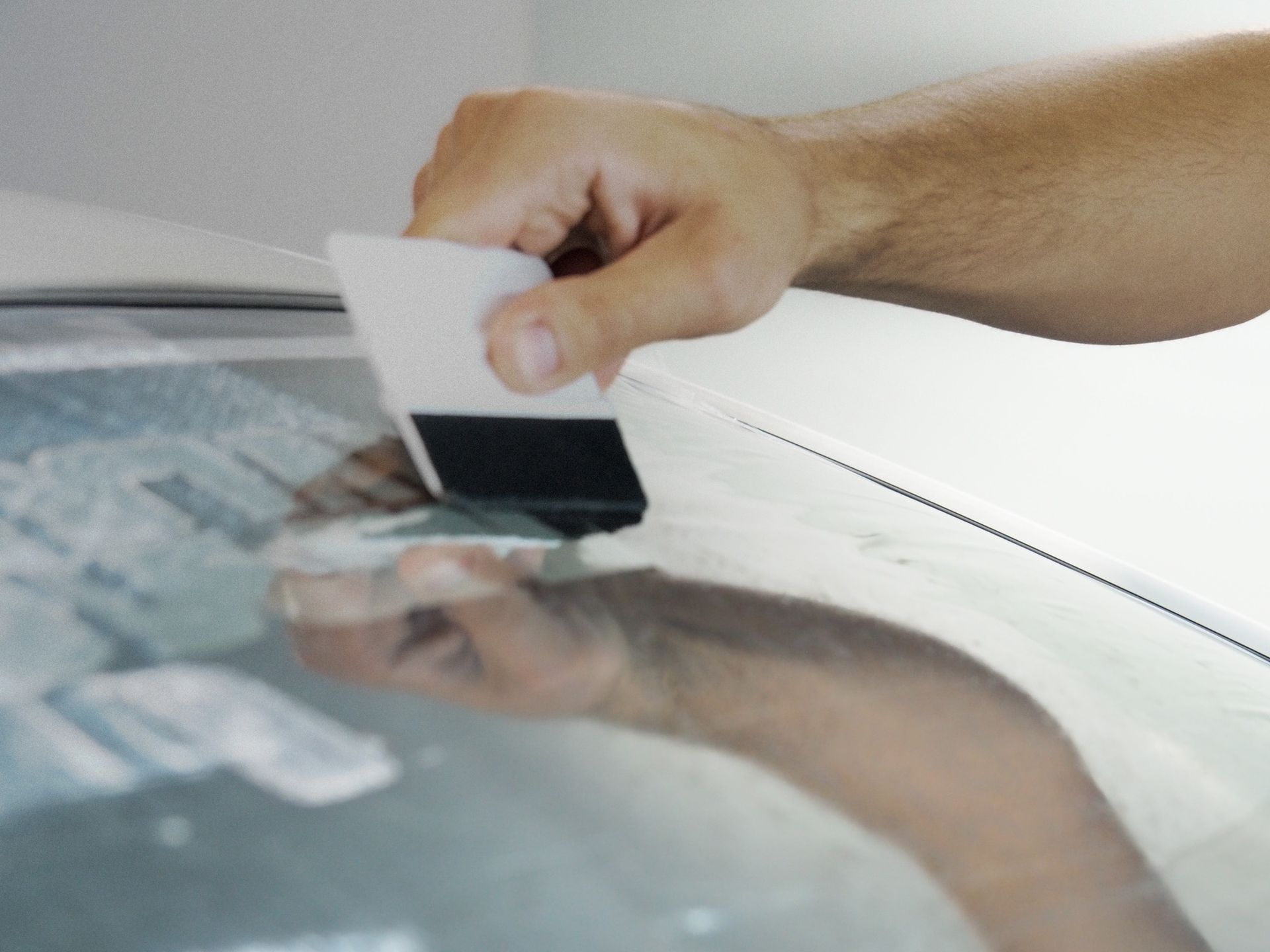 Hand using a squeegee to smooth a reflective surface, likely applying a film.