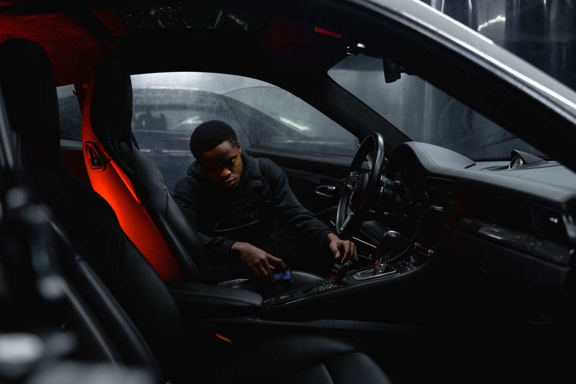 Man sitting in a car interior with red accent lighting, looking down at the center console