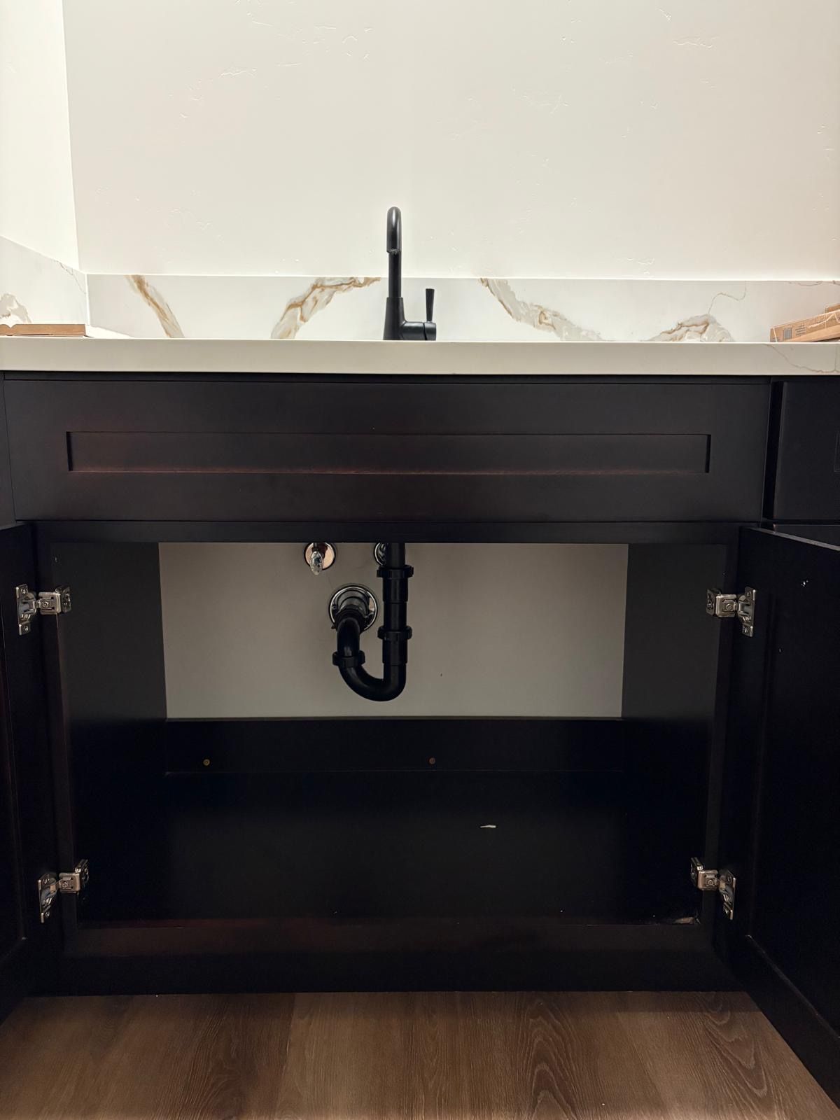 Bathroom sink cabinet with open doors, showing plumbing and countertop.