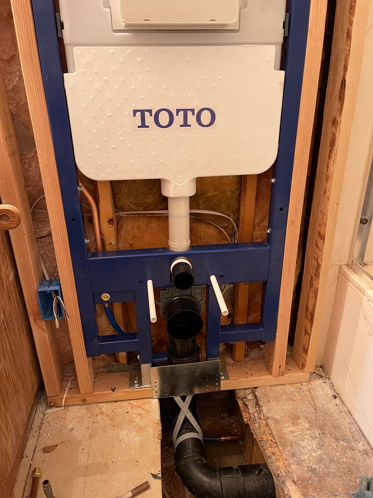 Framed TOTO toilet fixture installed in a bathroom wall. Black drainpipe and water lines are visible.