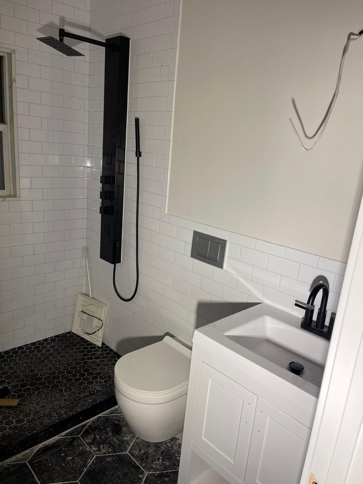 Modern bathroom with white tiled shower, black shower panel, toilet, vanity.