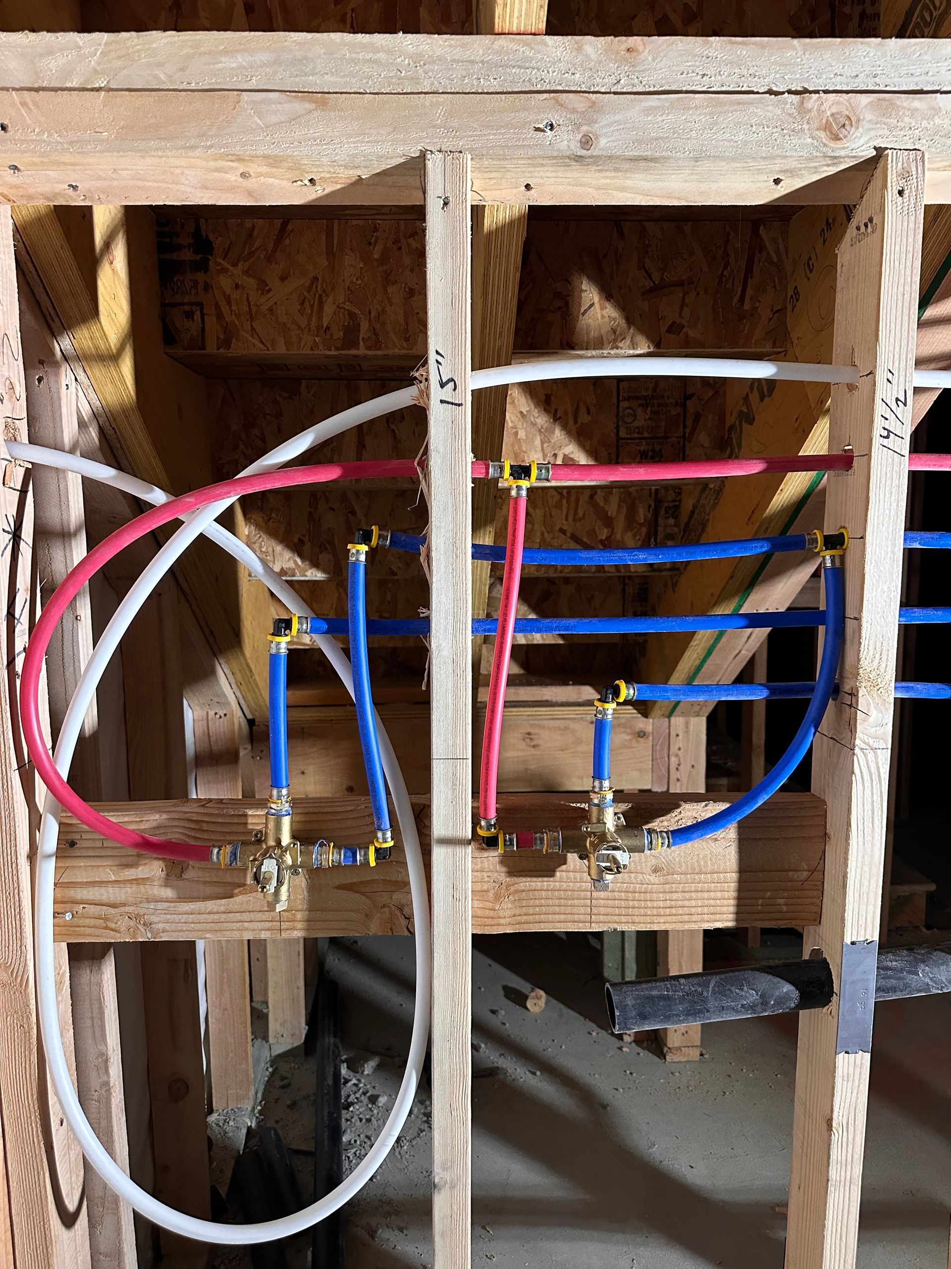PEX plumbing pipes (red, blue, white) in wooden wall framing, likely a bathroom water supply.
