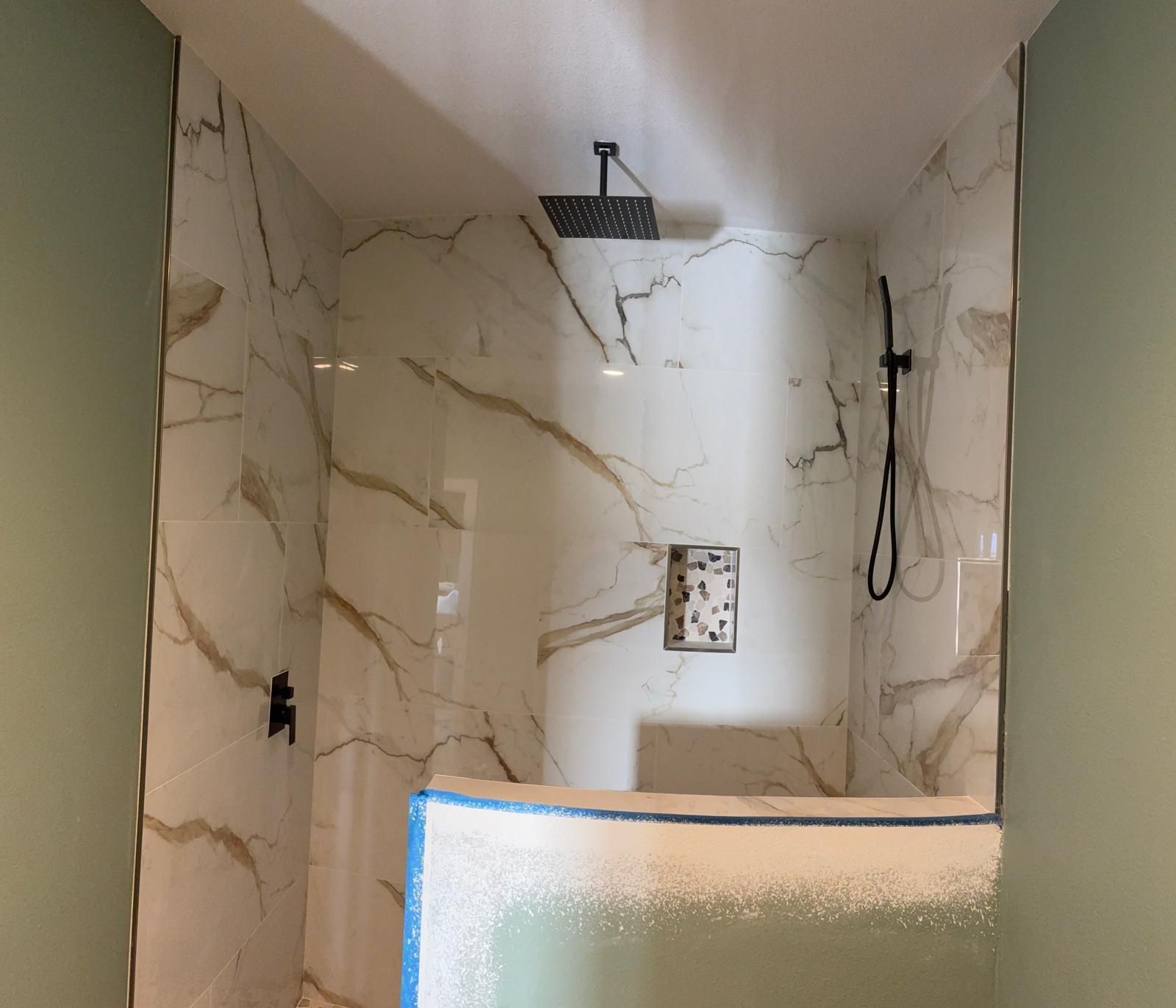 A shower stall with marble-patterned tiles, black fixtures, and a low bench.