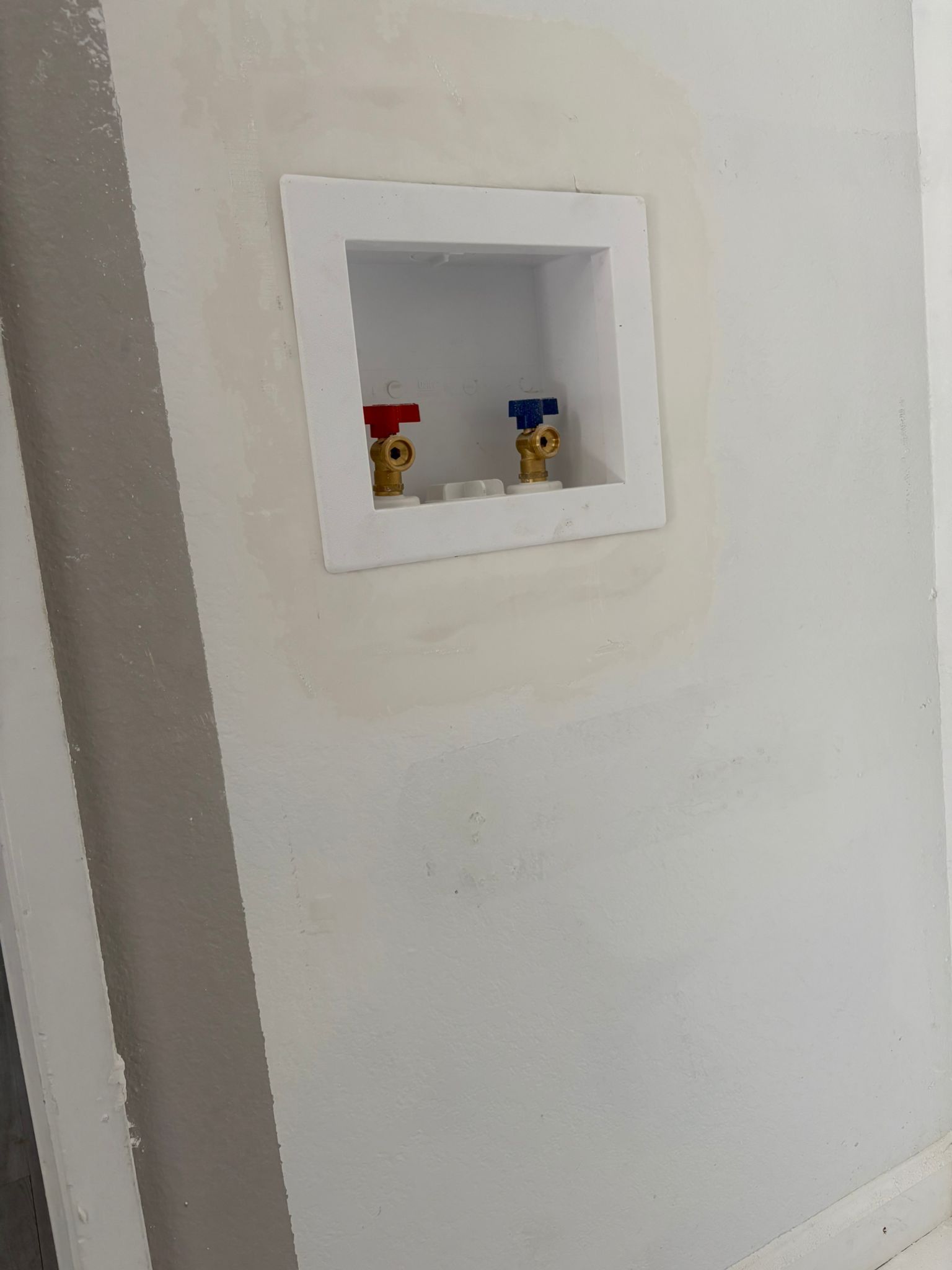 White laundry hookup box with red and blue water valves on a wall.