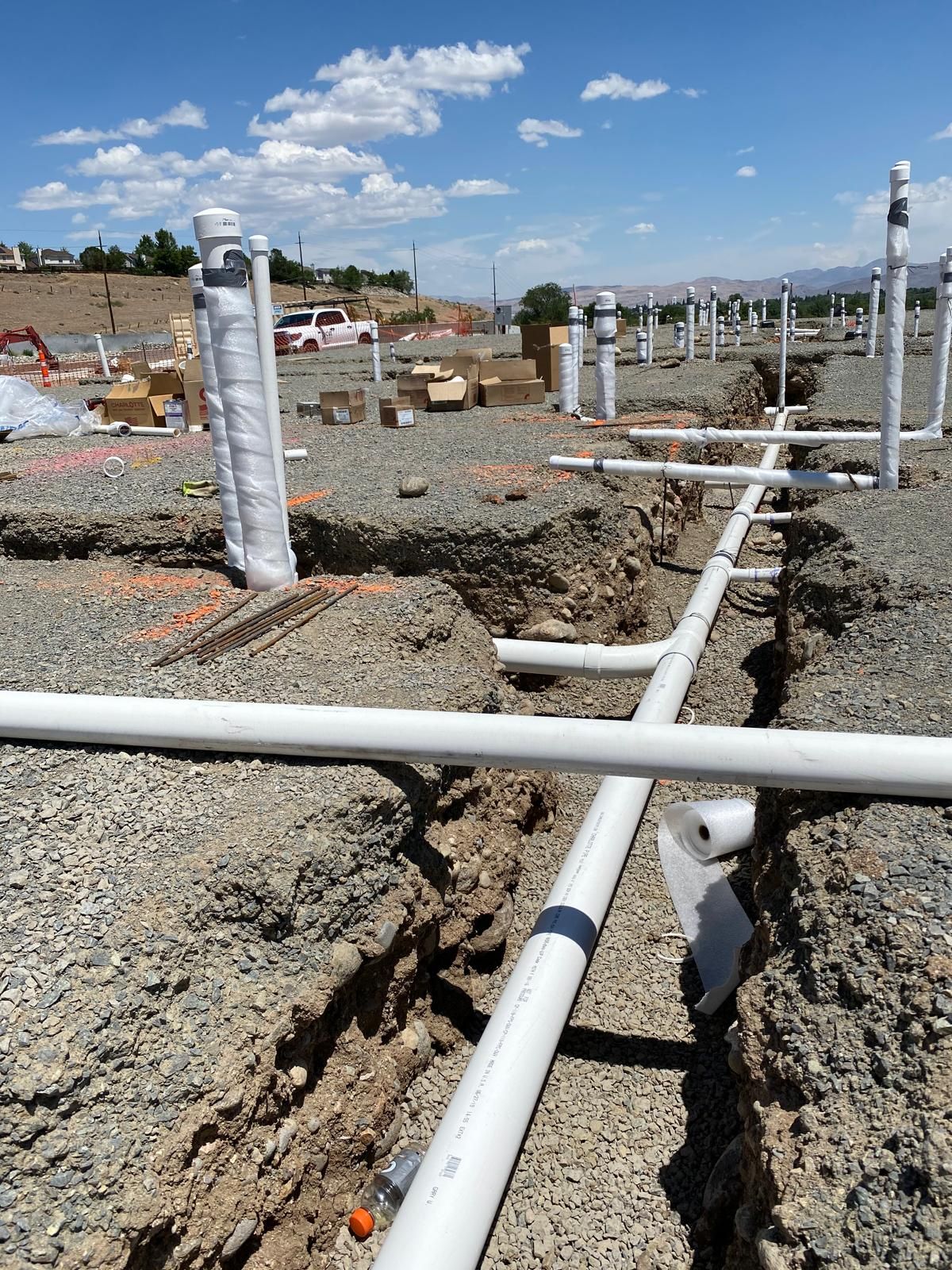 White PVC pipes in trenches, under construction, outdoors. Blue sky, rocky ground.