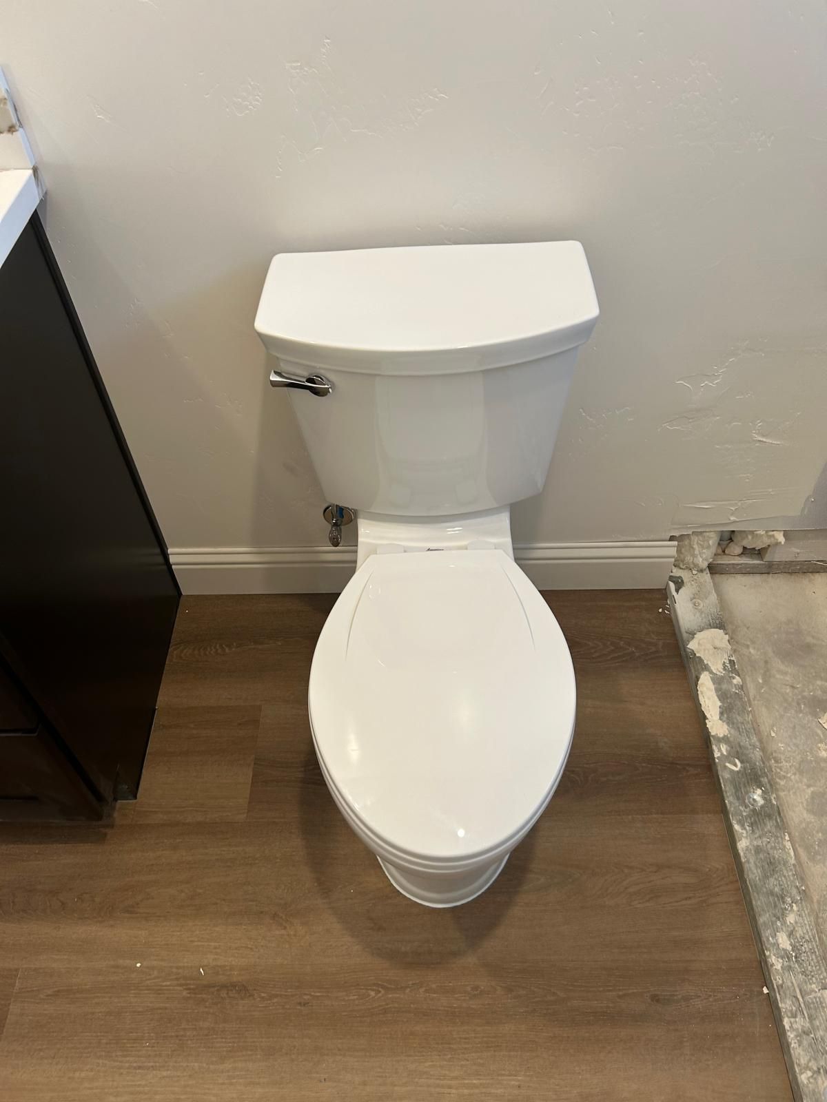 A white toilet is sitting on a wooden floor in a bathroom.