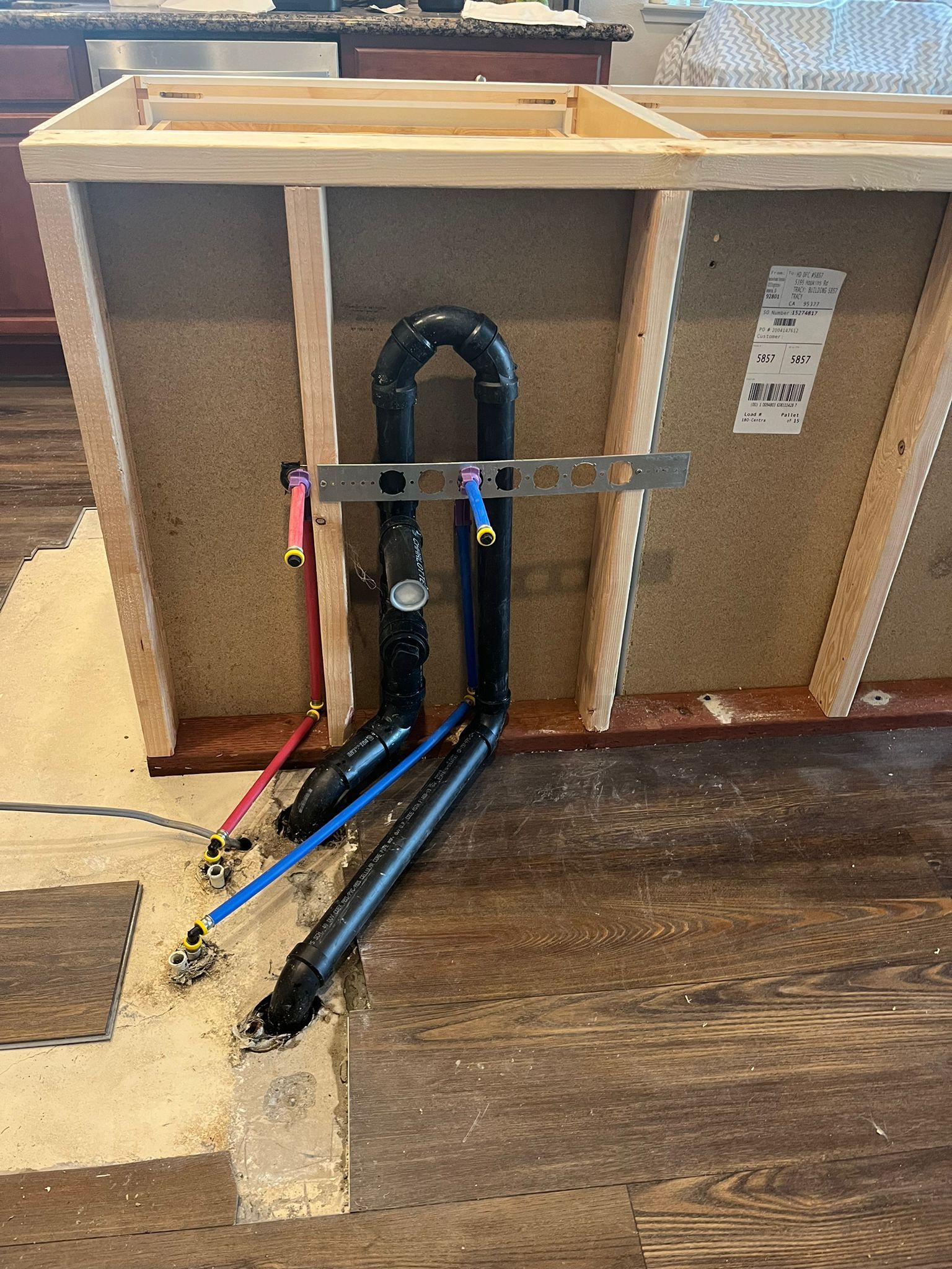 Plumbing under a kitchen sink with black pipes and water lines; level in place.