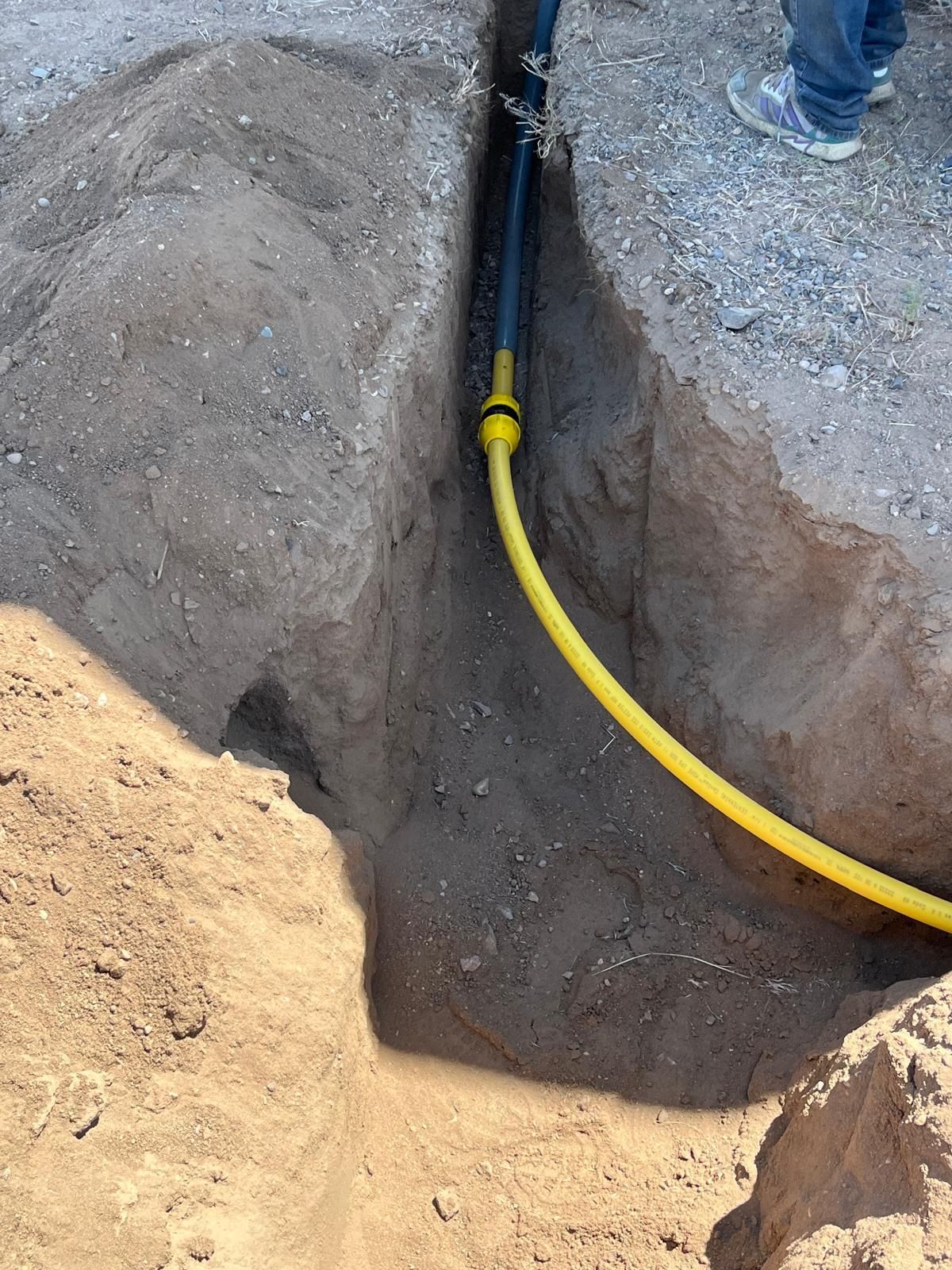 Yellow gas line in a dirt trench, likely for underground installation.
