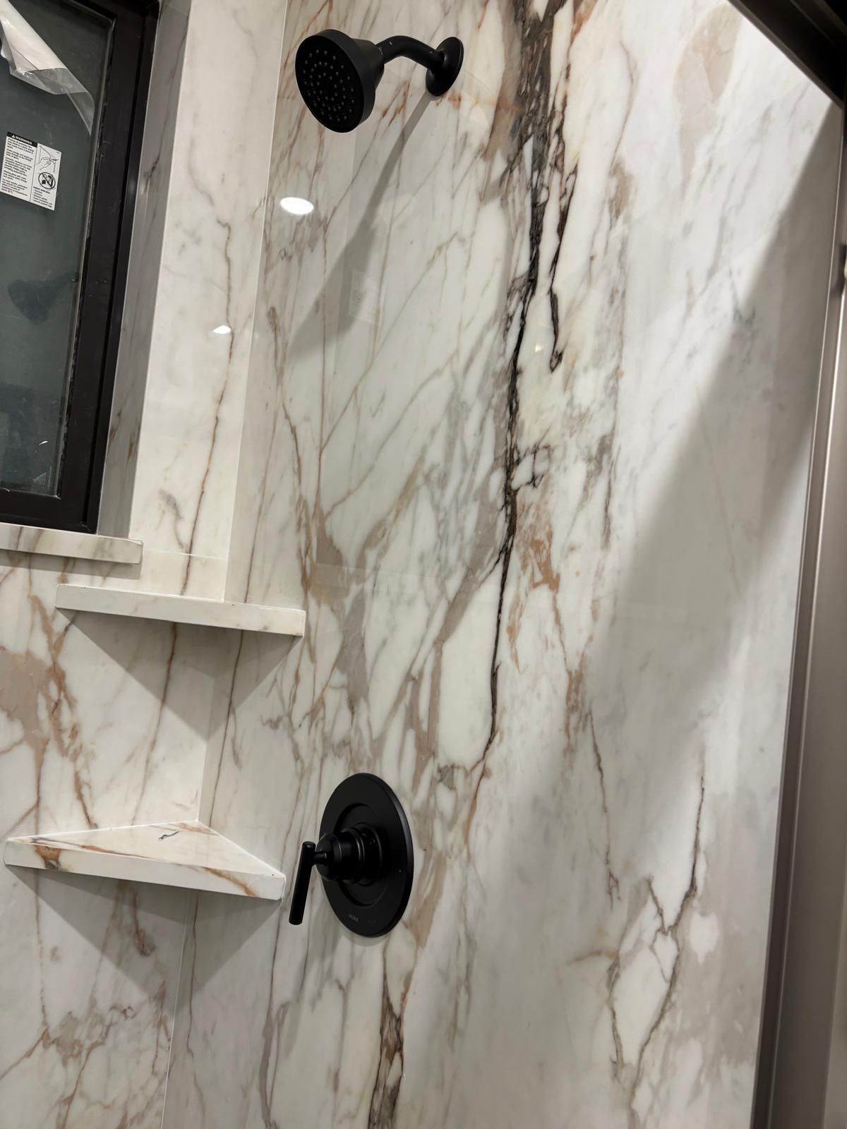 Shower with black fixtures and marble-patterned walls; built-in shelves.