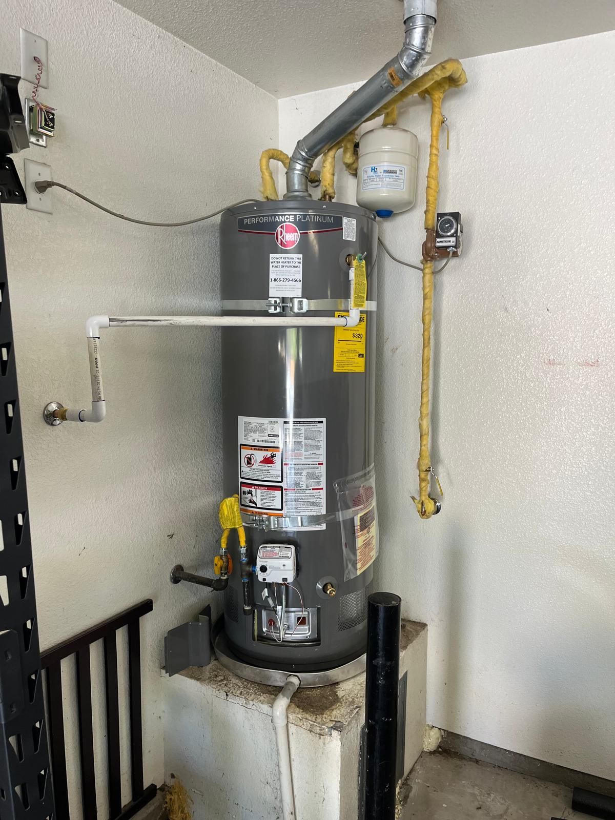 A gas water heater is sitting in a room next to a wall.