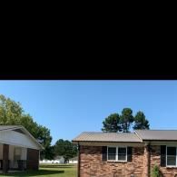 Suburban houses under a clear blue sky, with trees and a grassy yard.