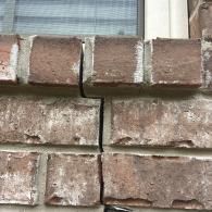 Cracked brick wall beneath a window sill, with visible mortar gaps and chipped bricks
