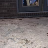 Concrete patio beside a brick wall and sliding glass door with a curtain visible inside.