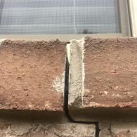 Close-up of cracked brown bricks with a vertical gap beneath a window frame.