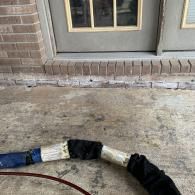 Concrete porch with a gray door and a black-and-white hose lying across the ground.