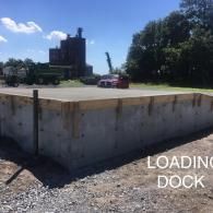 Concrete loading dock platform with trucks and a car in a sunny industrial lot