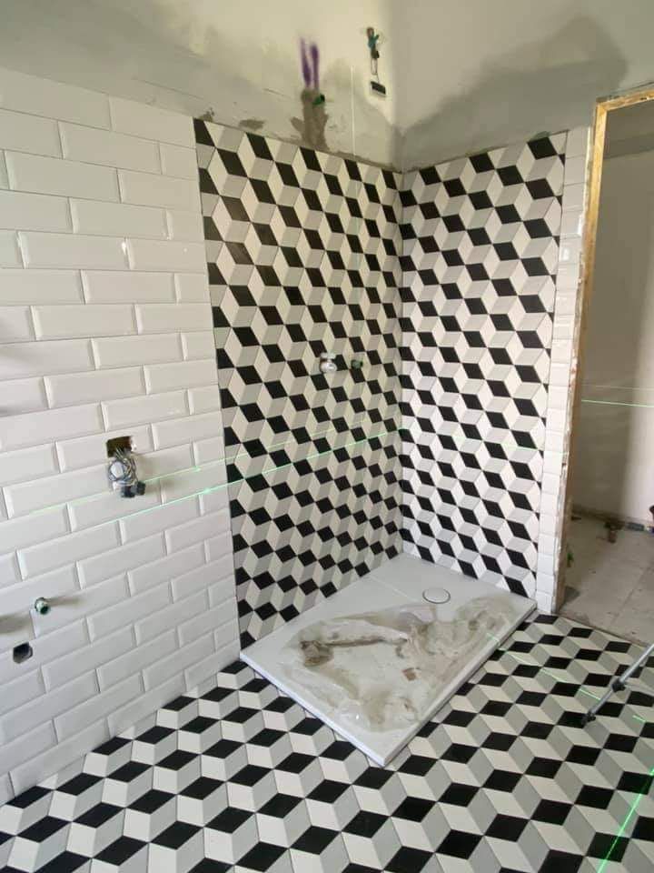 Un bagno in fase di ristrutturazione caratterizzato da una parete con motivo a mattoni bianchi e piastrelle geometriche a forma di cubo 3D in bianco e nero sul pavimento.
