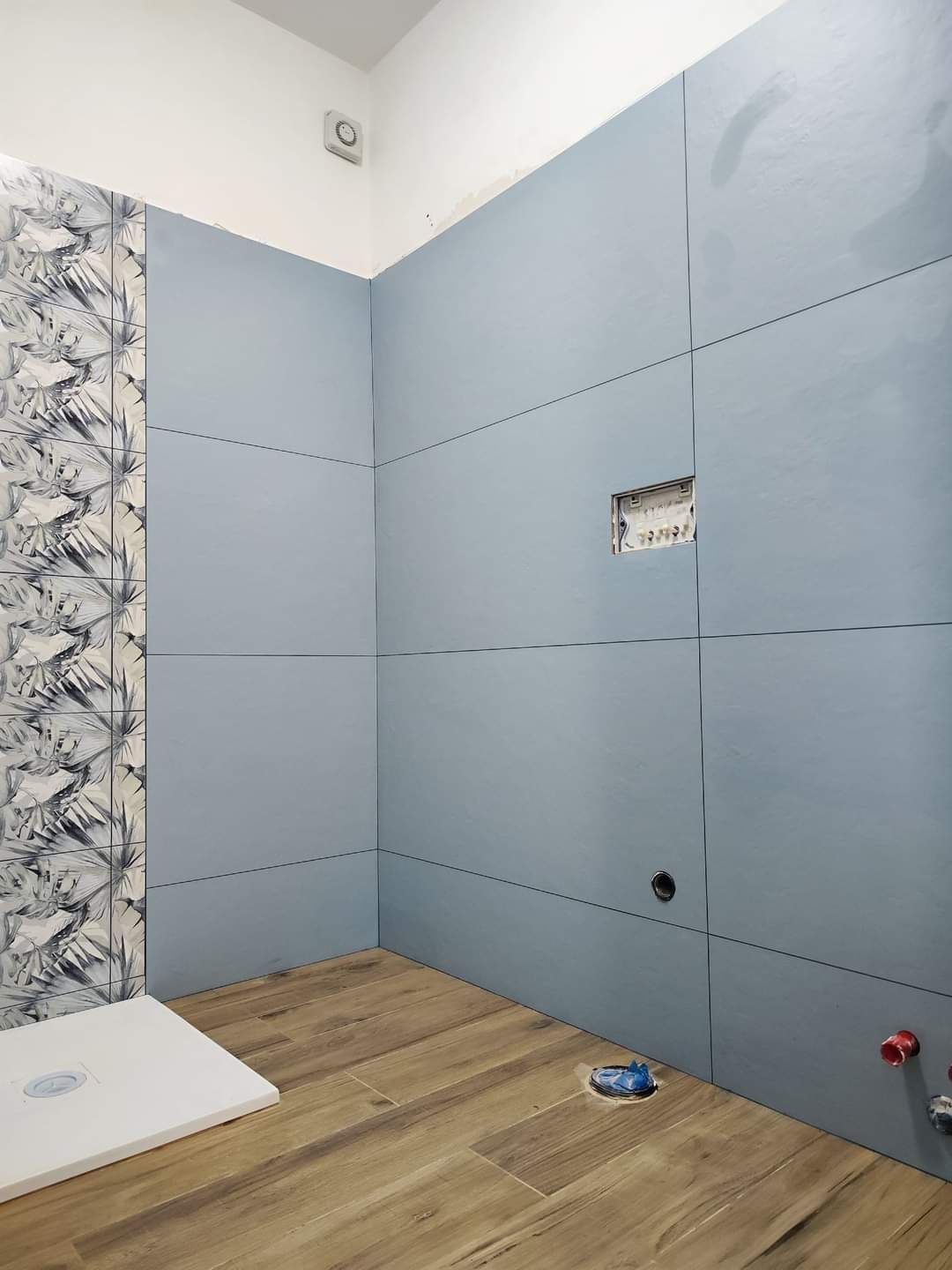 Un bagno in fase di ristrutturazione con grandi piastrelle azzurre a parete, una fascia decorativa a motivi geometrici e pavimento piastrellato effetto legno.