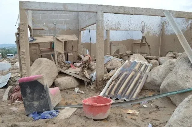 Flood and storm damage inside a partially destroyed building with debris, mud, and damaged roofing materials.