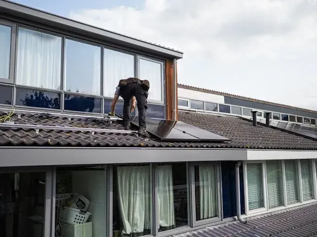 Professional roofer installing or repairing a tiled residential roof on a modern house exterior.