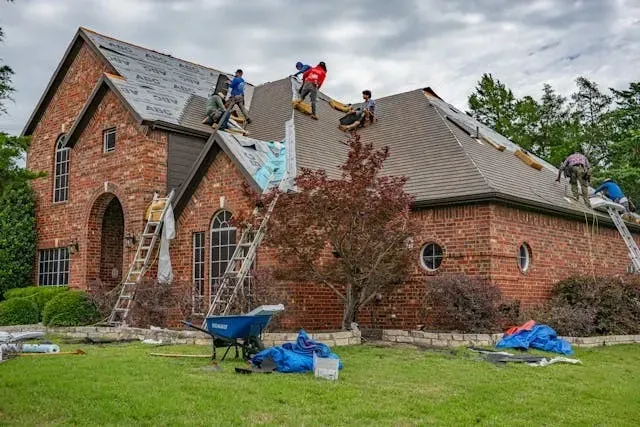 Professional roofing crew performing residential roof installation and shingle replacement on a brick house.