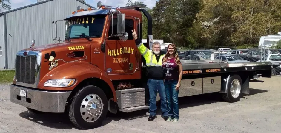 Orange and black tow truck with two people standing beside it in a parking lot