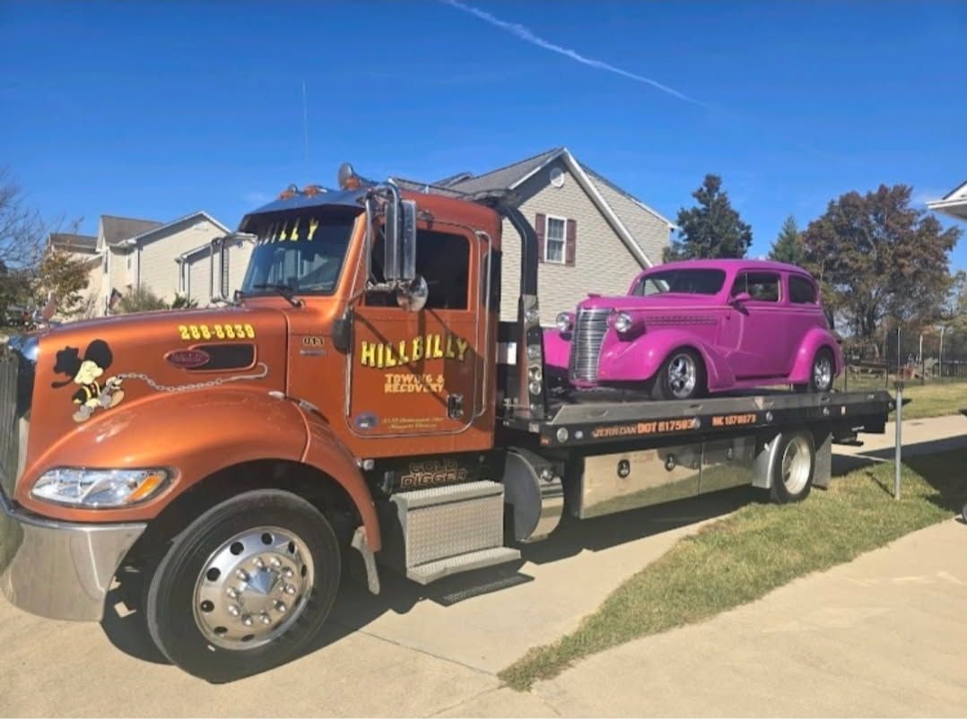 Red Hillbilly tow truck parked outdoors with a ladder and an ATV on the bed