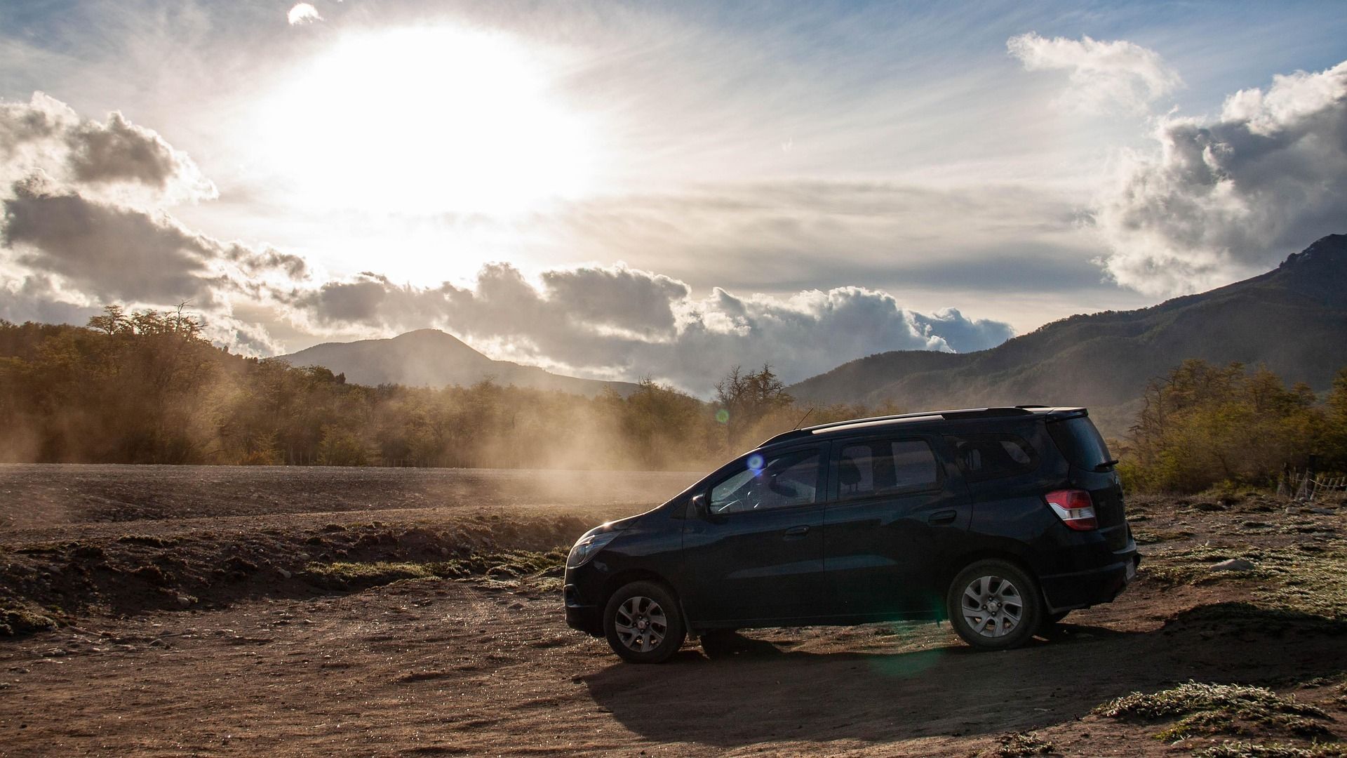 Una camioneta Chevrolet Spin negra está estacionada en un campo de tierra con montañas al fondo.
