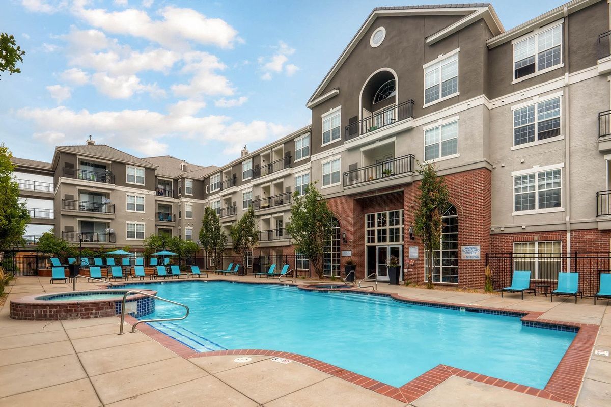 Apartment building with a large pool and hot tub, blue chairs around pool at The Viridian in Greenwood Village, CO.