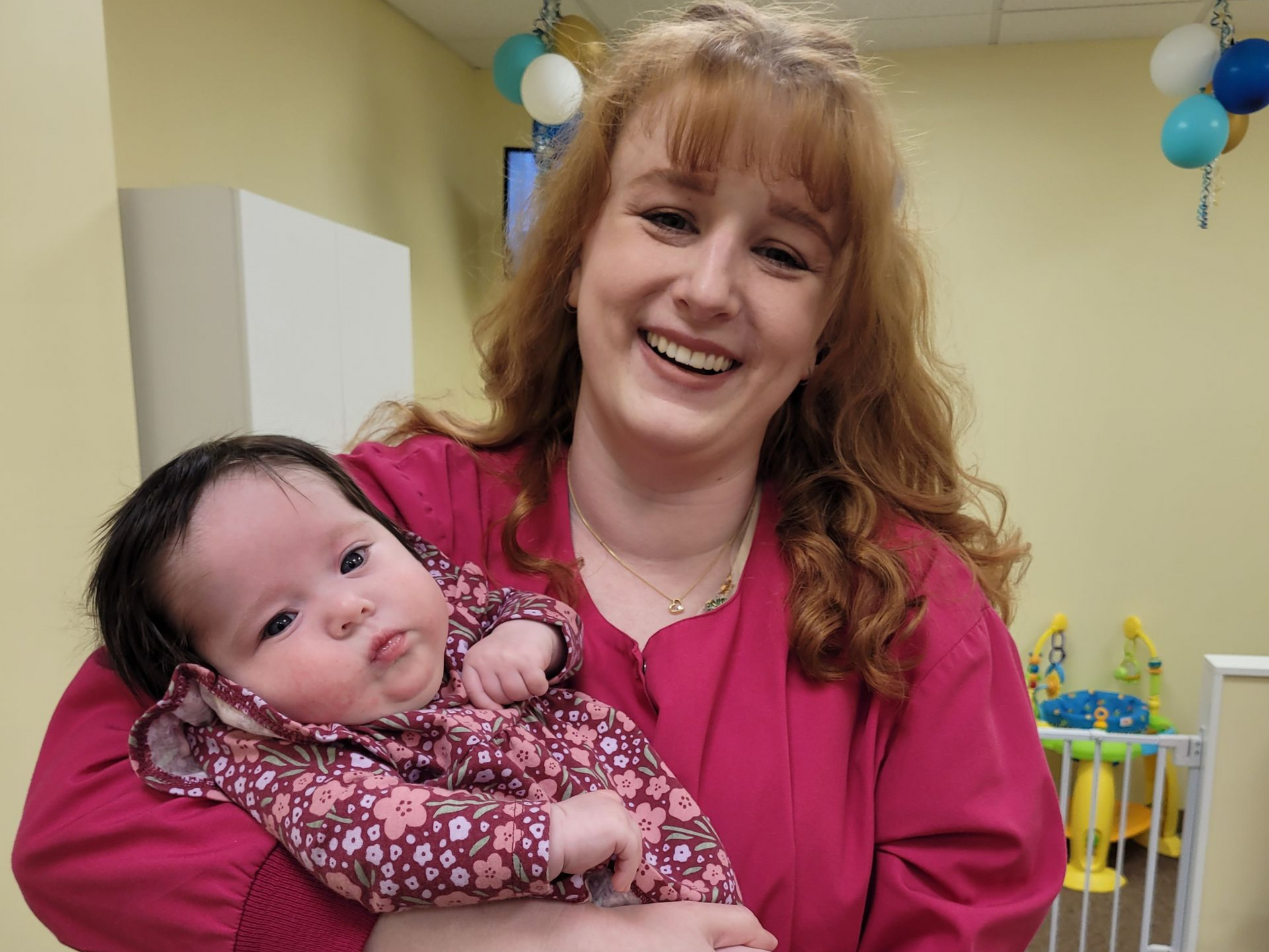 Woman in a pink top holding a baby at a cheerful indoor celebration