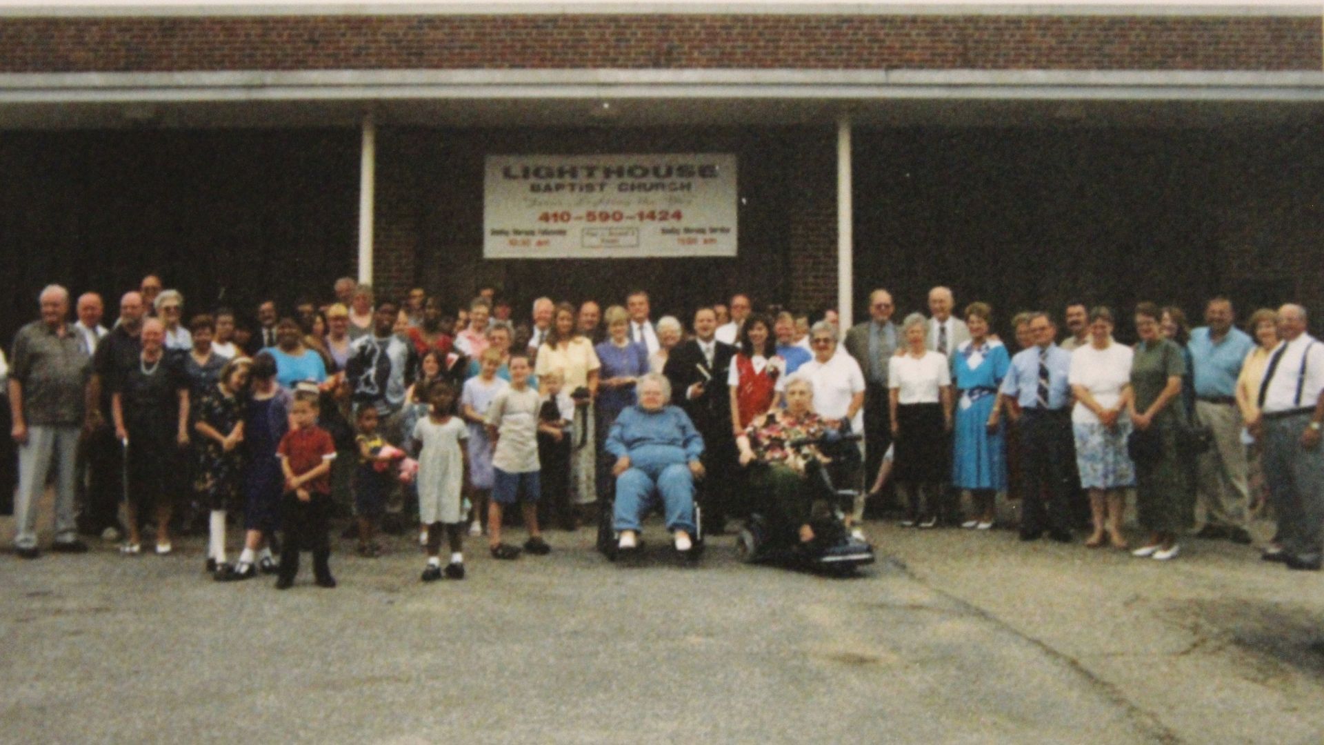 Large group posing outside a building entrance, with a sign above the doorway.