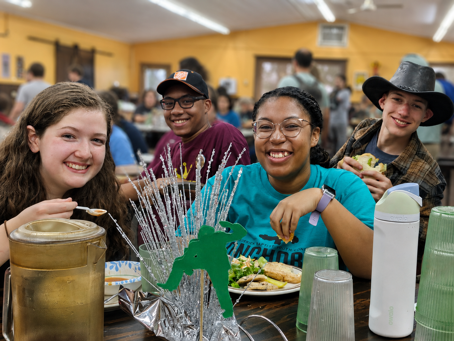 Group of friends smiling at a table with drinks and plates at a casual indoor gathering.