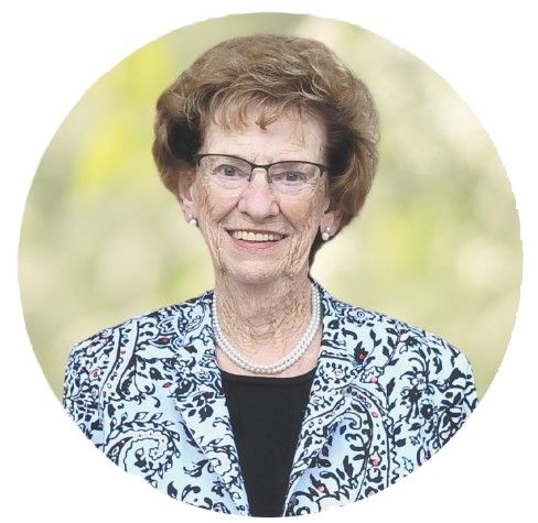 Smiling woman in glasses and patterned jacket, posed against a soft green background.