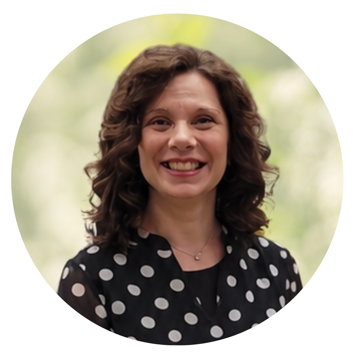 Smiling woman with curly hair in a black polka-dot blouse against a blurred green background