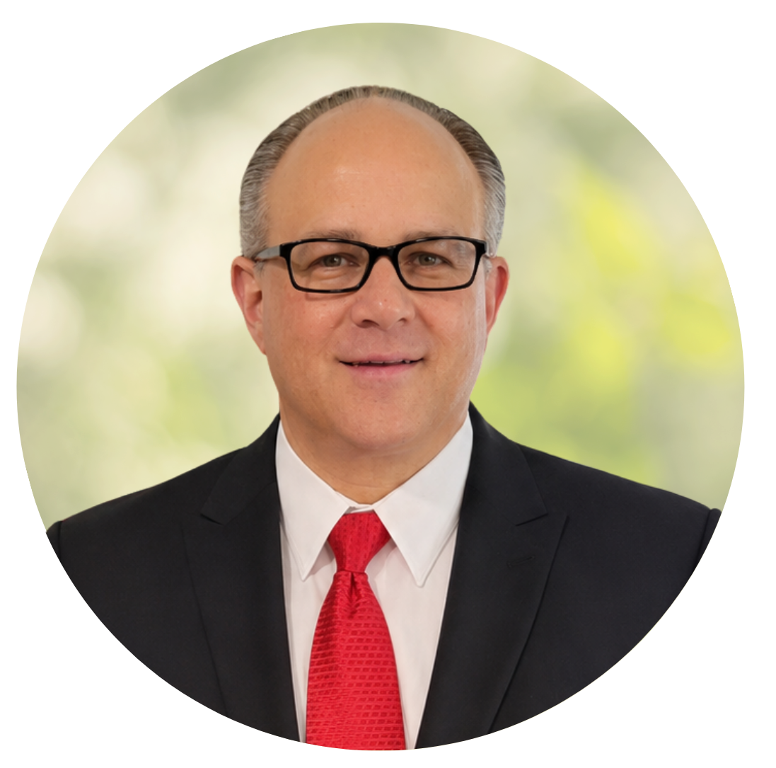 Headshot of a man in a black suit, white shirt, and red tie, wearing glasses, against a soft green background