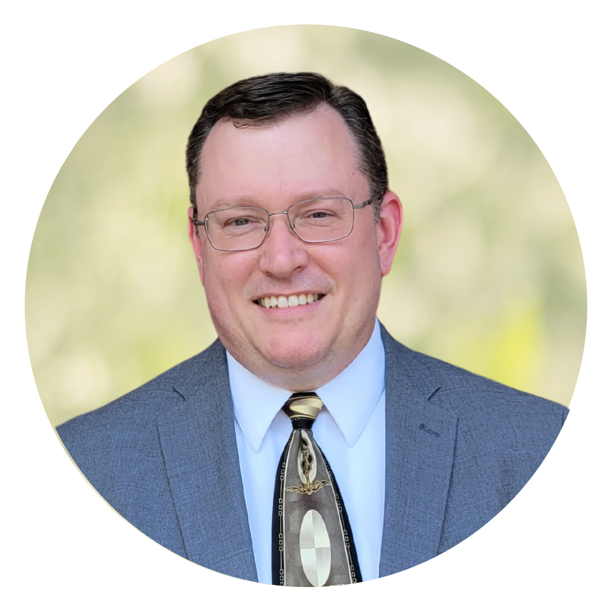 Portrait of a smiling man in glasses wearing a blue suit and patterned tie on a soft green background