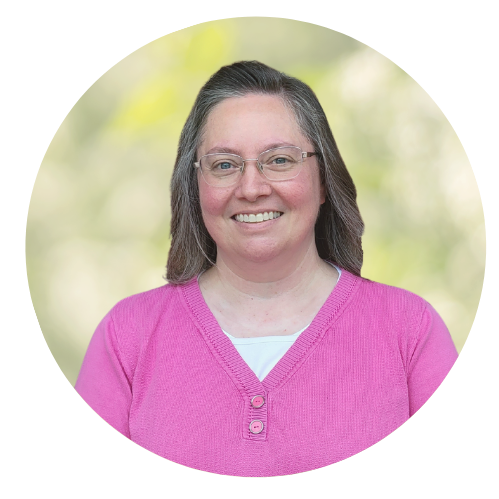 Smiling woman in glasses wearing a pink sweater against a blurred green background