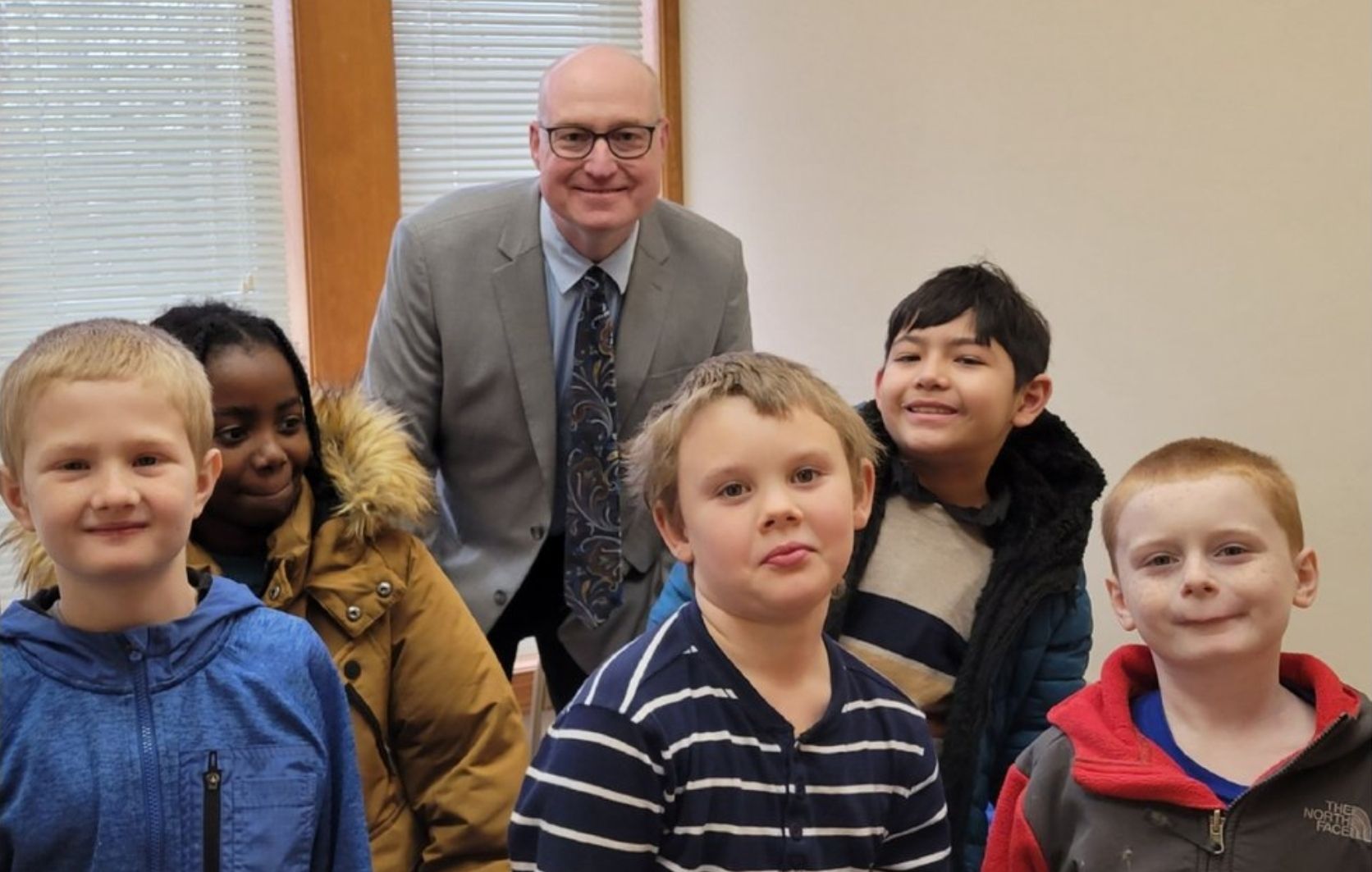 Man in a suit standing with five smiling children indoors
