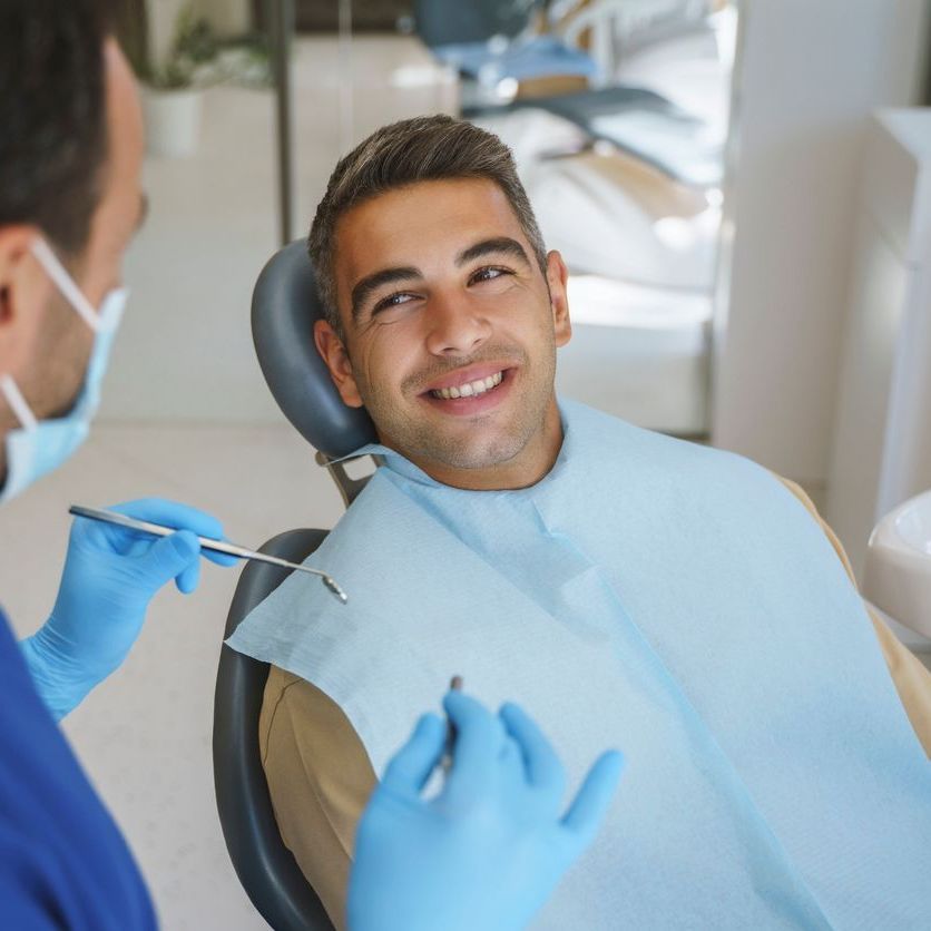 Man smiles during a dental check-up. Dentist in blue gloves and mask holds tools, office setting.