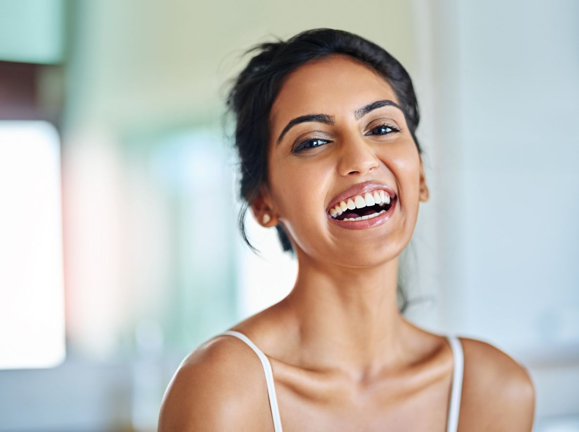 Woman with dark hair smiling widely, wearing a white tank top.