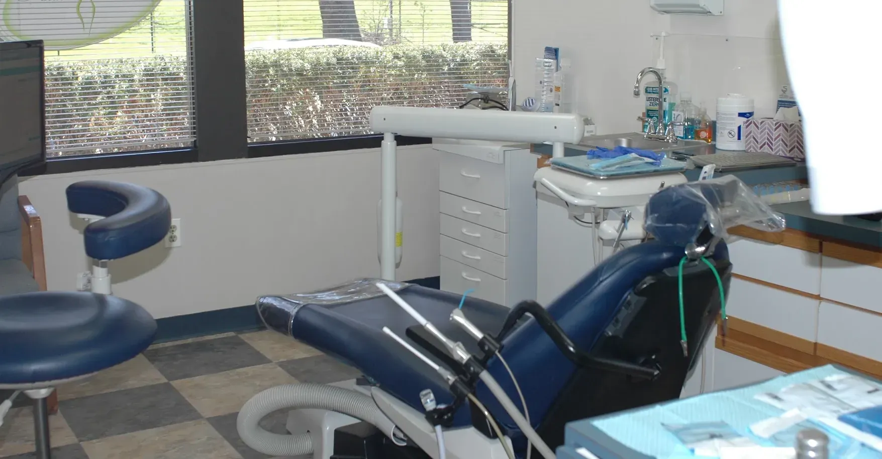 Dentist's office interior: blue dental chair, instruments, window, and cabinetry.