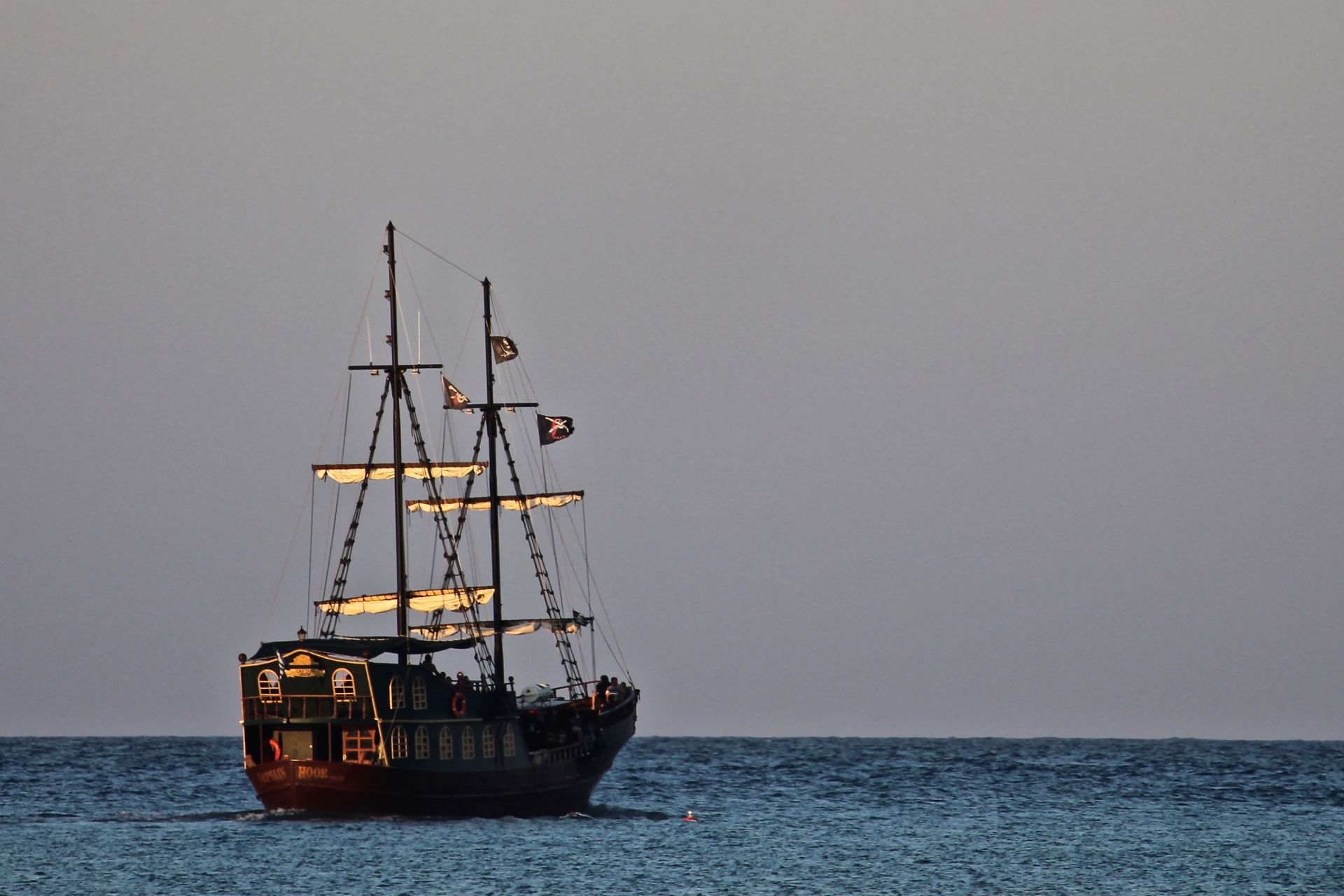 Sailing ship silhouetted on calm blue sea at dusk under a grey sky