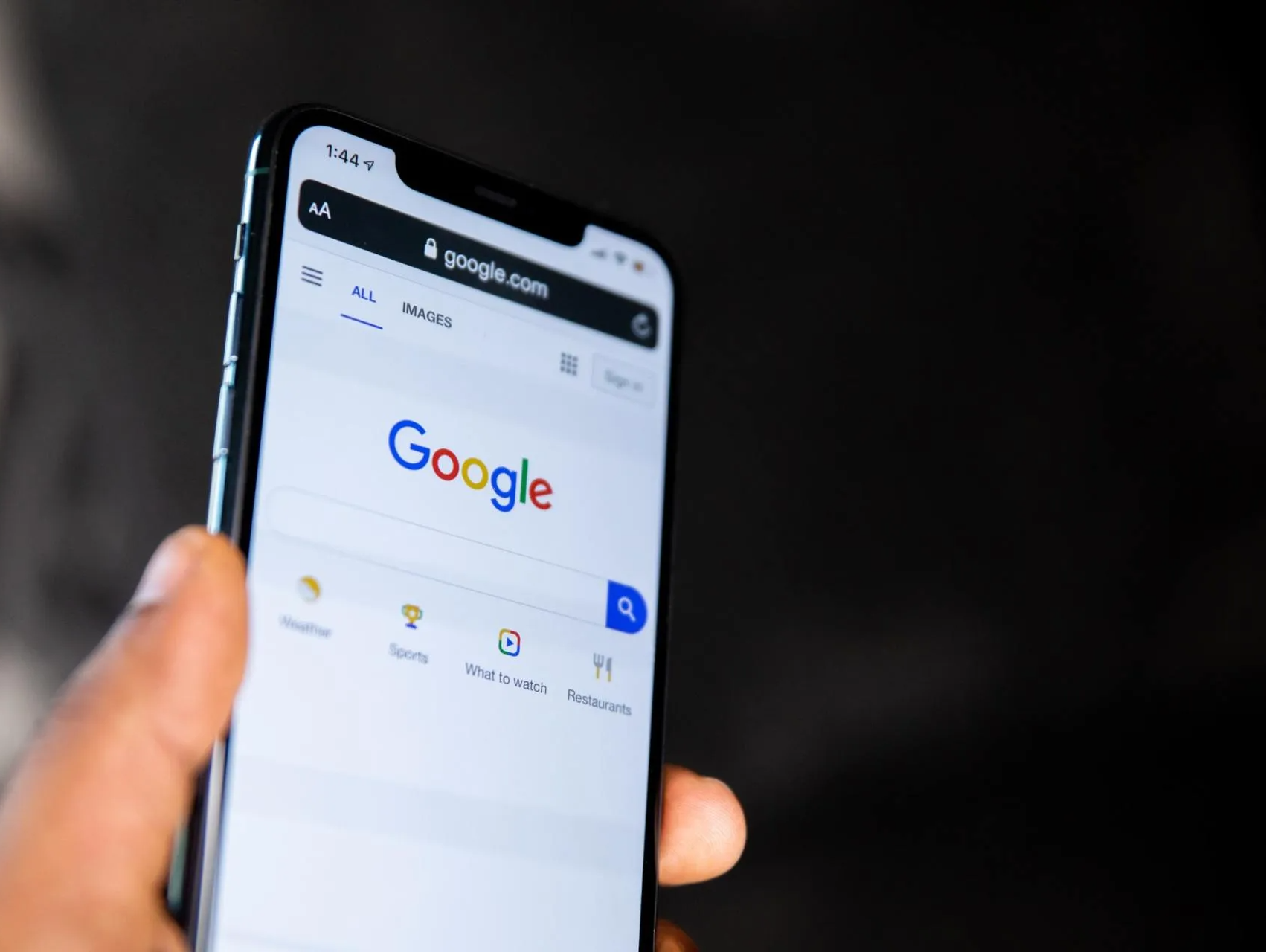 A person is holding a cell phone with the google search page open.