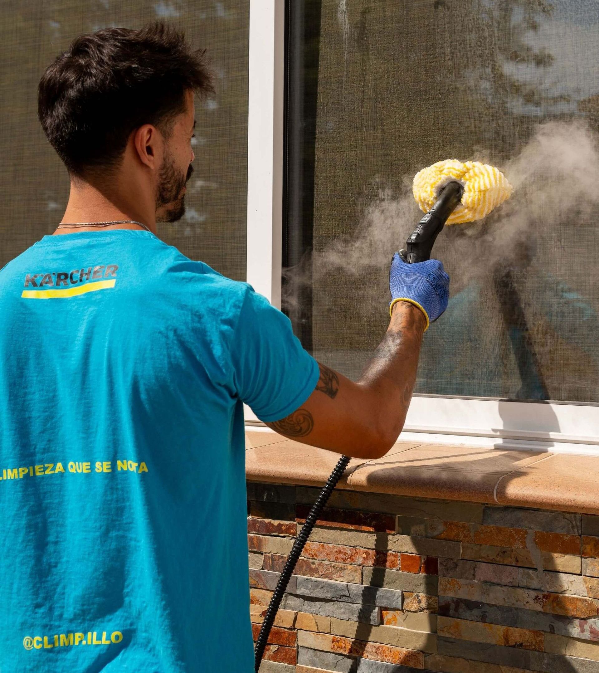 Un hombre con una camisa azul está limpiando una ventana con un limpiador a vapor.