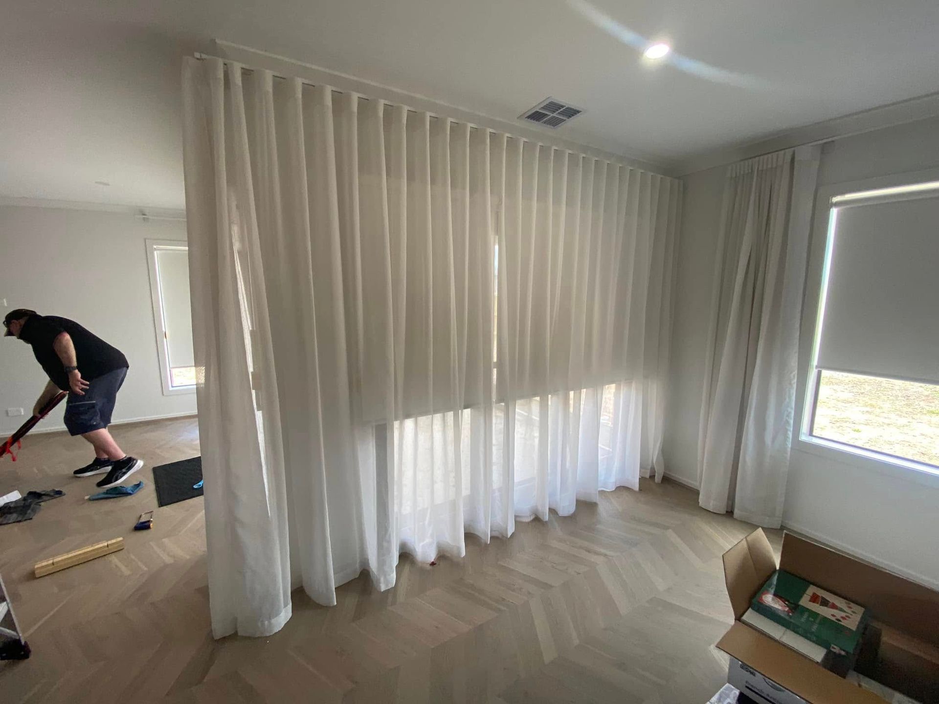 A Man Is Standing In A Room With White Curtains And Blinds — Night & Day Blinds and Awnings in Pakenham, VIC