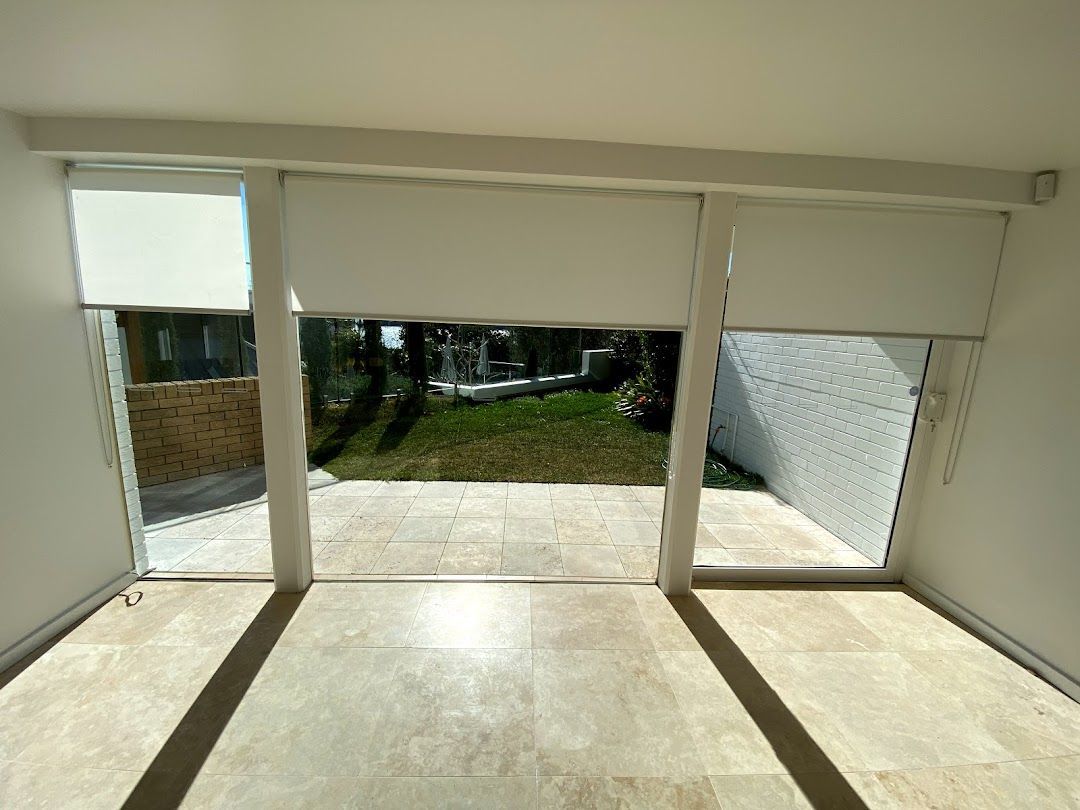 White Roller Blinds Are Covering A Window In A Room — Night & Day Blinds and Awnings in Pakenham, VIC